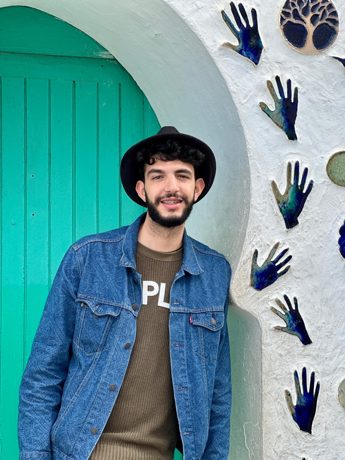 Moha beside a bright green arched door on a whitewashed Marrakech wall of ceramic hands