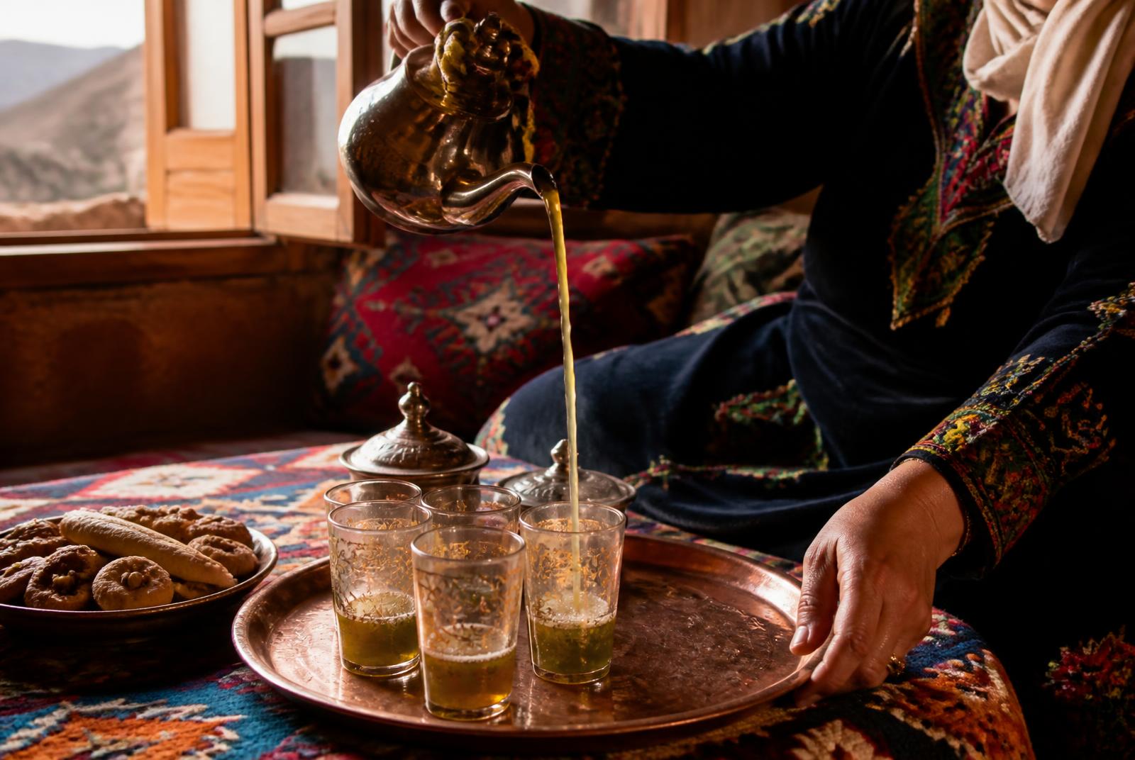 Mint tea poured from a copper pot into glasses on a handwoven rug in a High Atlas village home