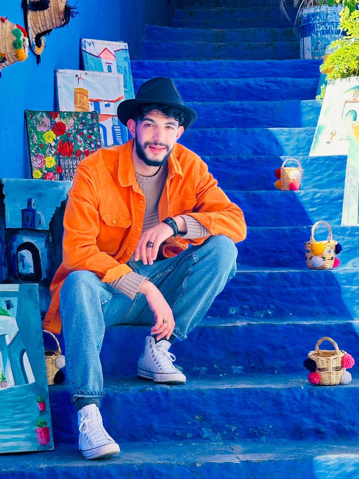 Moha sitting on the blue-washed steps of Chefchaouen among handwoven baskets, Morocco