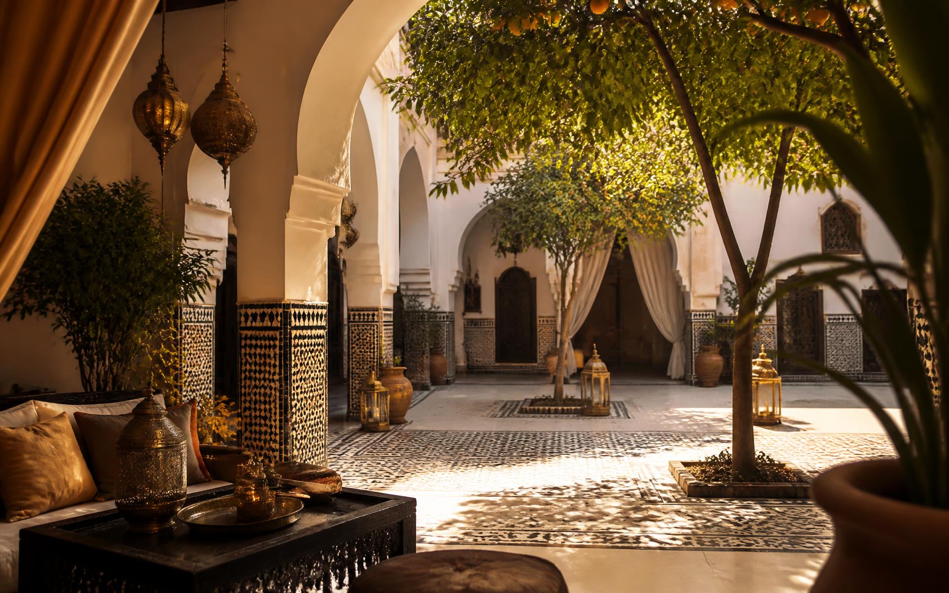 Morning light entering a Marrakech riad courtyard with horseshoe arches, zellige tiles and brass lanterns