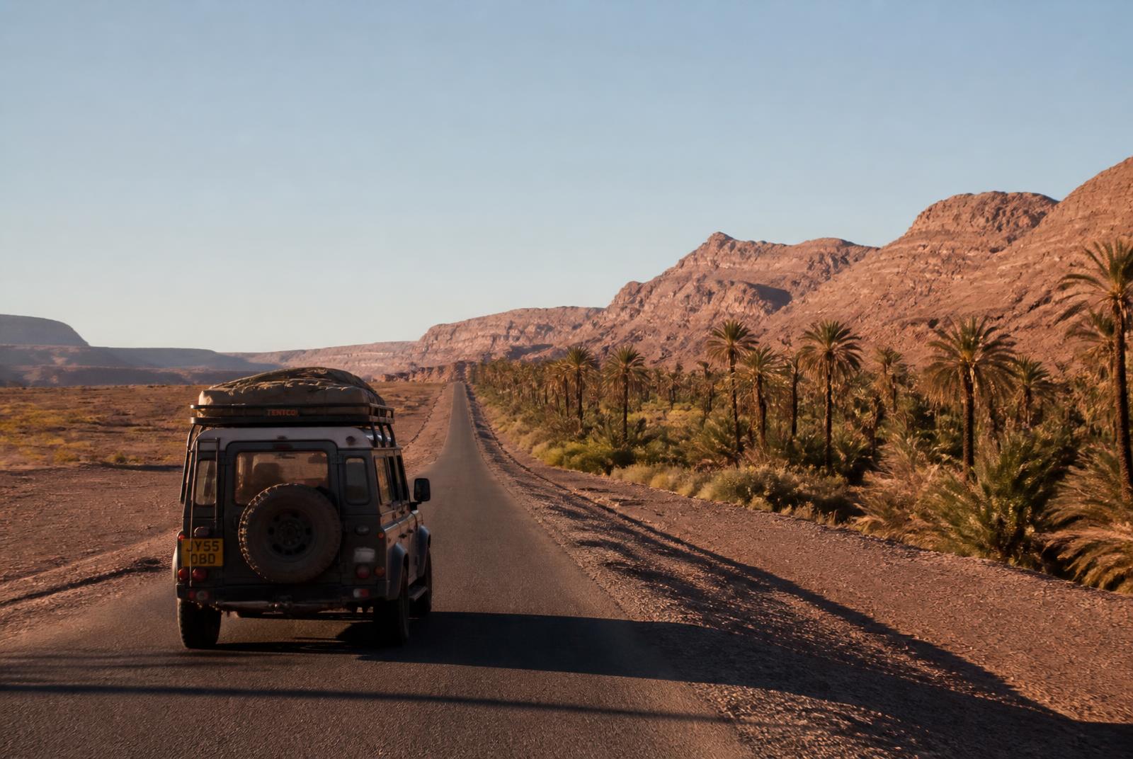 Private 4x4 on an empty desert road through the Draa Valley palm groves in southern Morocco