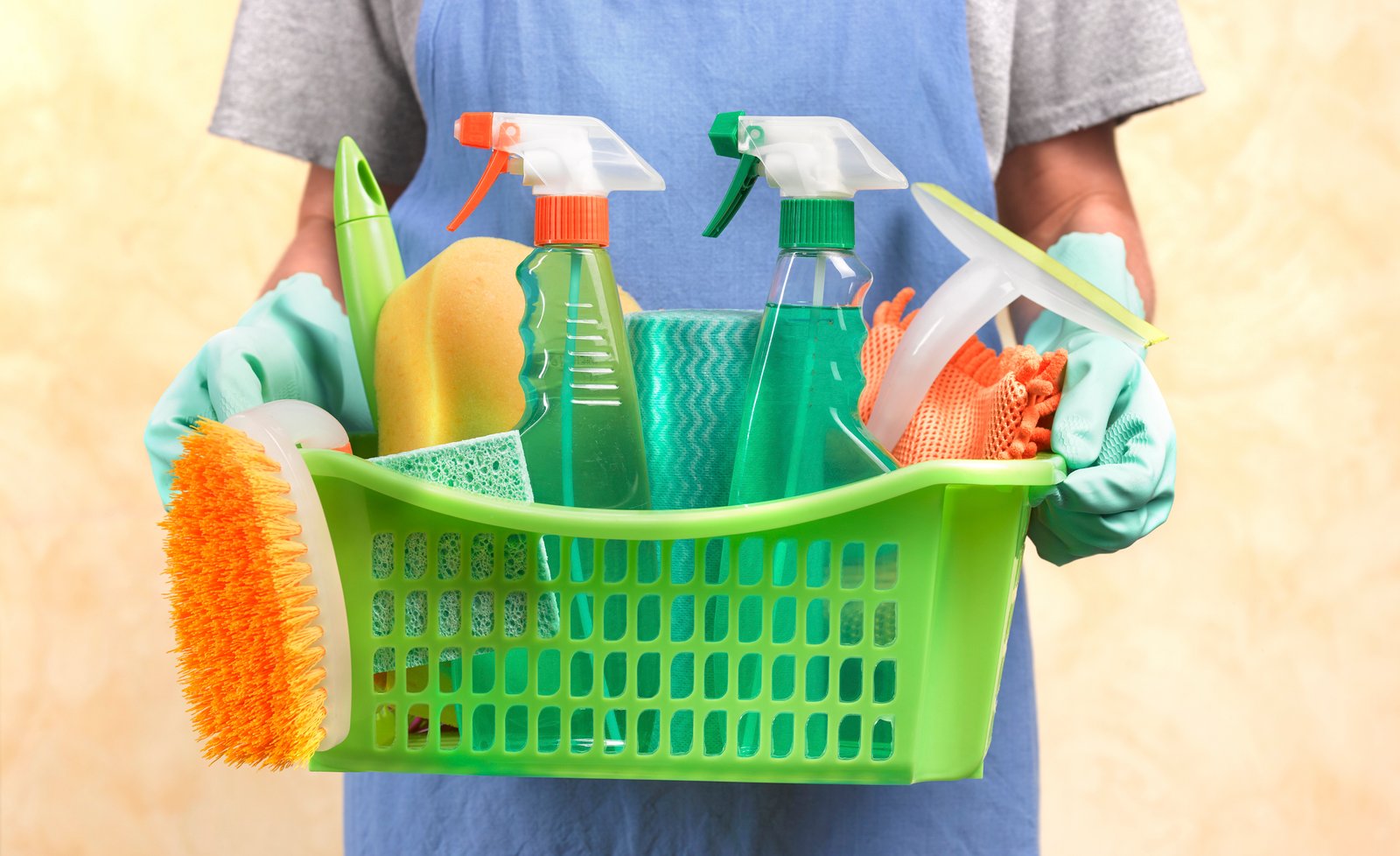 Close up of a woman holding a basket containing cleaning materials.